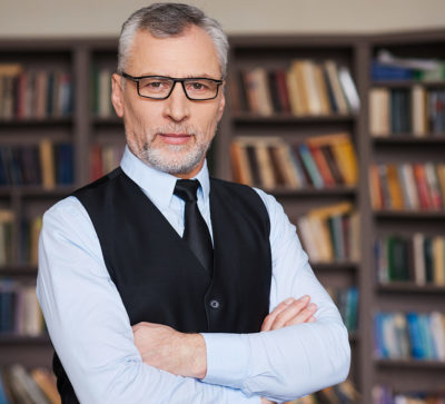 Accounting professor with glasses looking at camera in front of a bookshelf