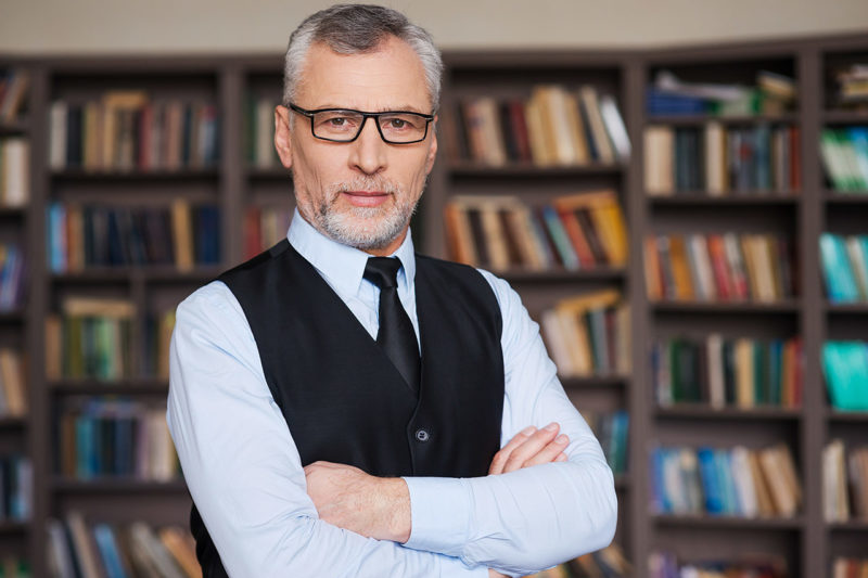 Accounting professor with glasses looking at camera in front of a bookshelf