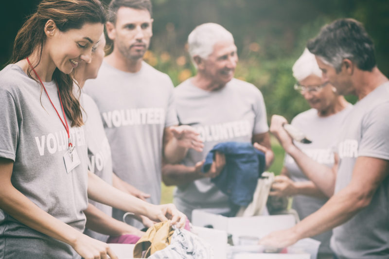 Multigenerational volunteers standing in circle outside, wearing grey tshirts