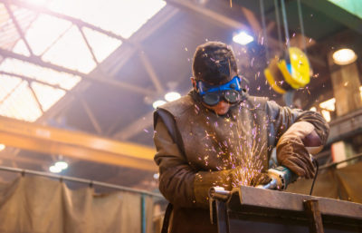 Young man with protective goggles welding in a factory