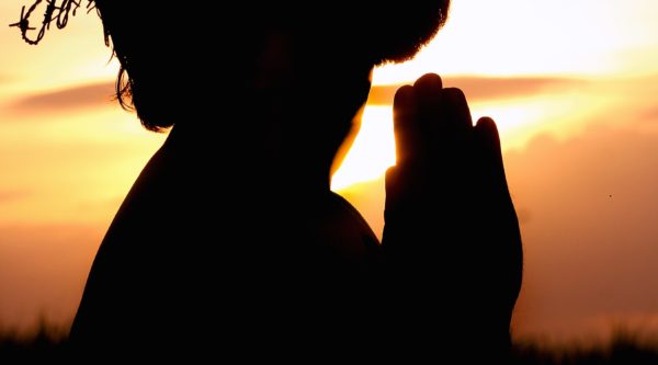 Silhouette image of person praying against setting sun