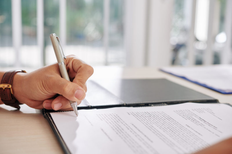 Hand of business person signing contract at desk in office